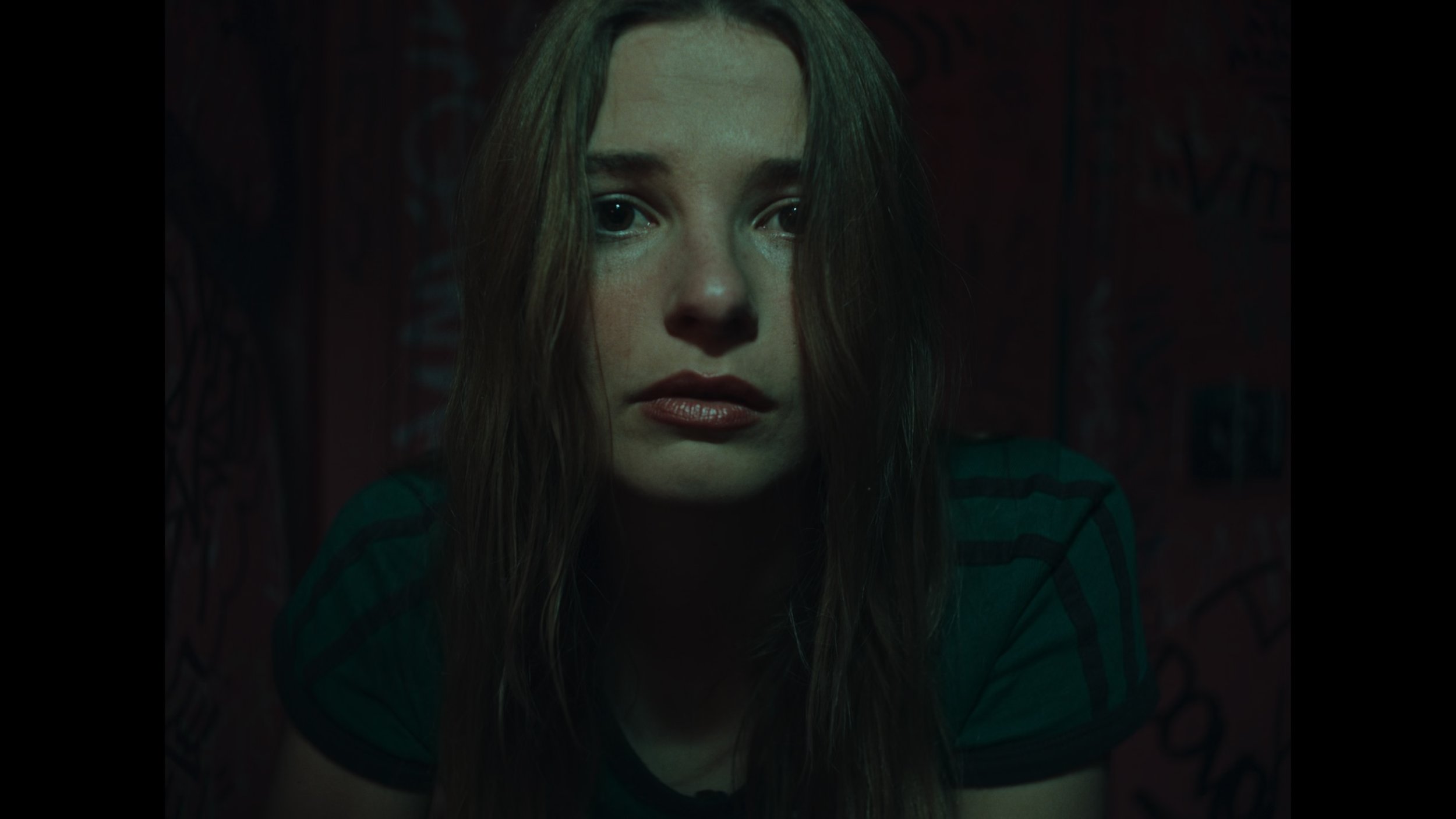 frame grab from the indie film Openers, woman washed in soft green light stares directly into camera as a conduit for a mirror, looks concerned