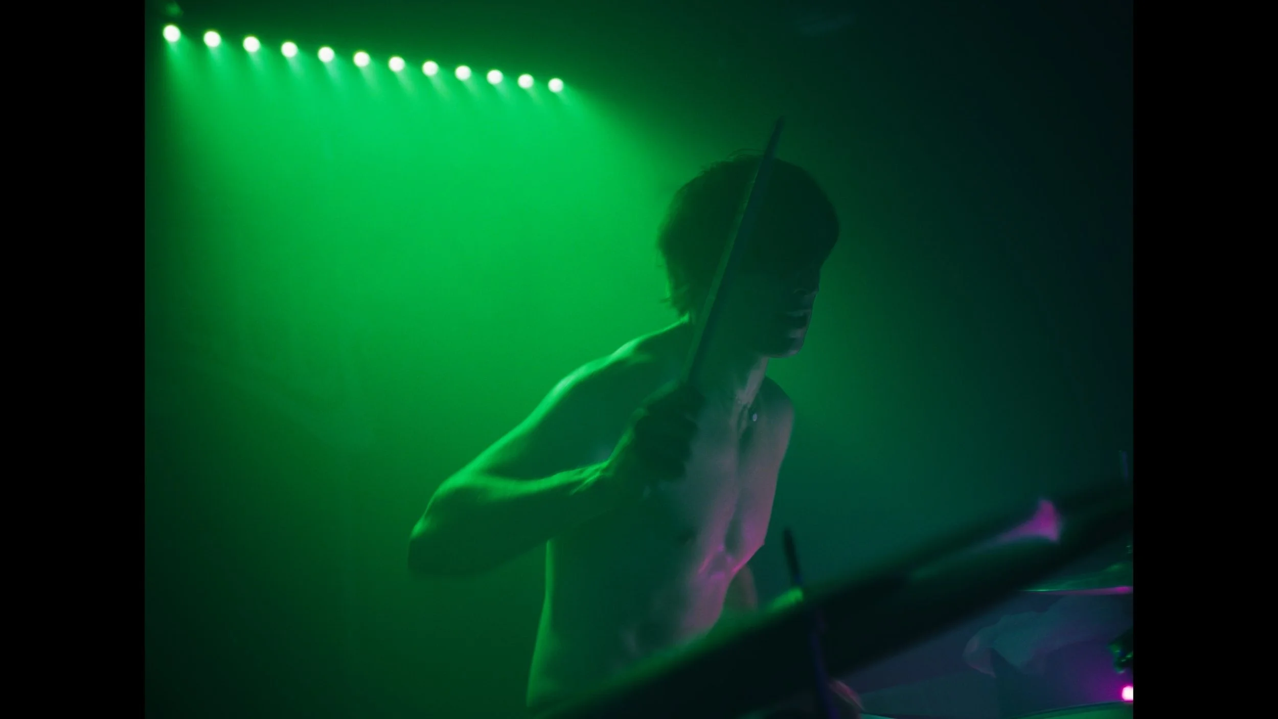 cinematic still frame from indie film, Openers, man washed in green stage light, plays drums
