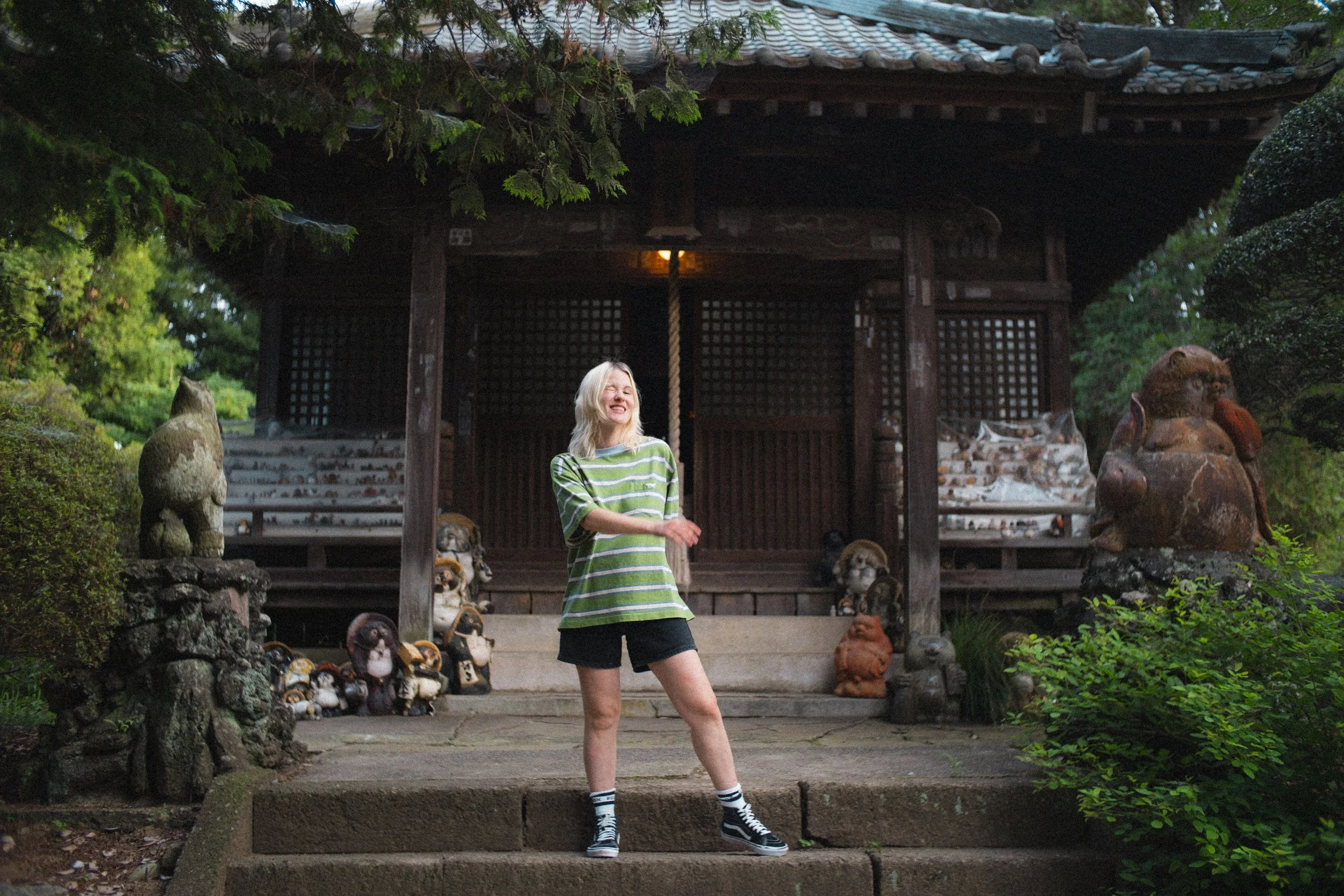 Cinematographer and photographer Ashton McKenzie makes a goofy face in front of a shrine in Japan, surrounded by tanuki statues.