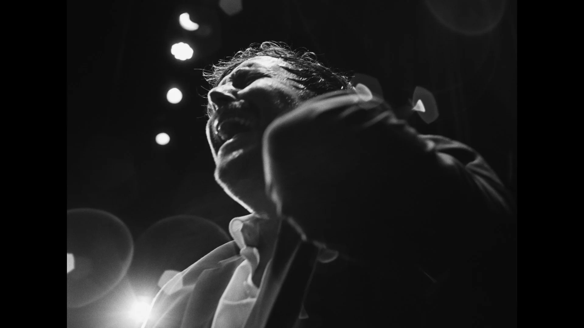 Music video frame grab, lead singer of Seattle rock band Gatsbys American dream, Nic Newsham, sings passionately in black and white with large lens flares