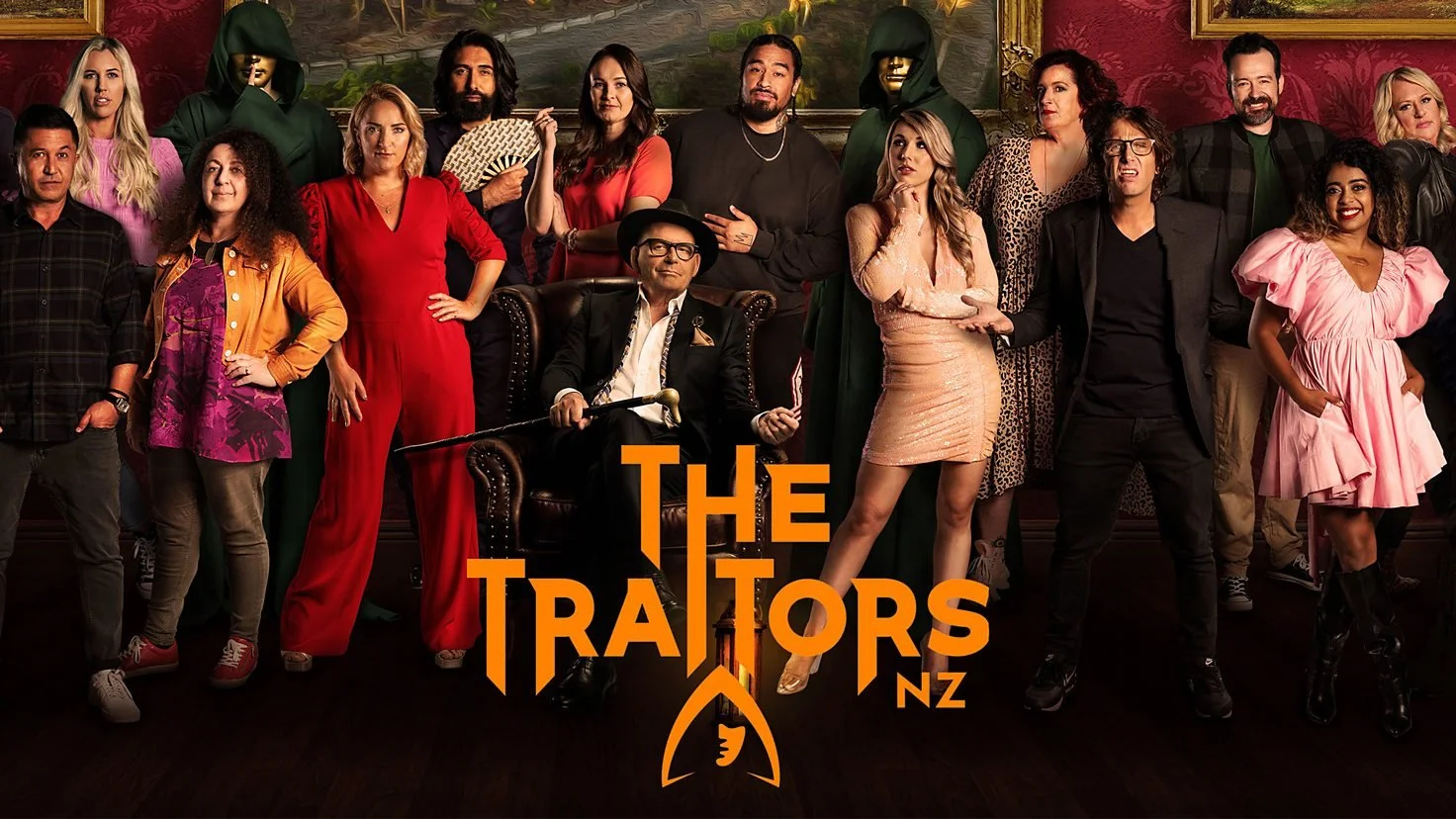 Group of people in formal attire posing for 'The Traitors NZ' show poster, with two figures in hooded cloaks and masks. Orange text reads 'The Traitors NZ.'