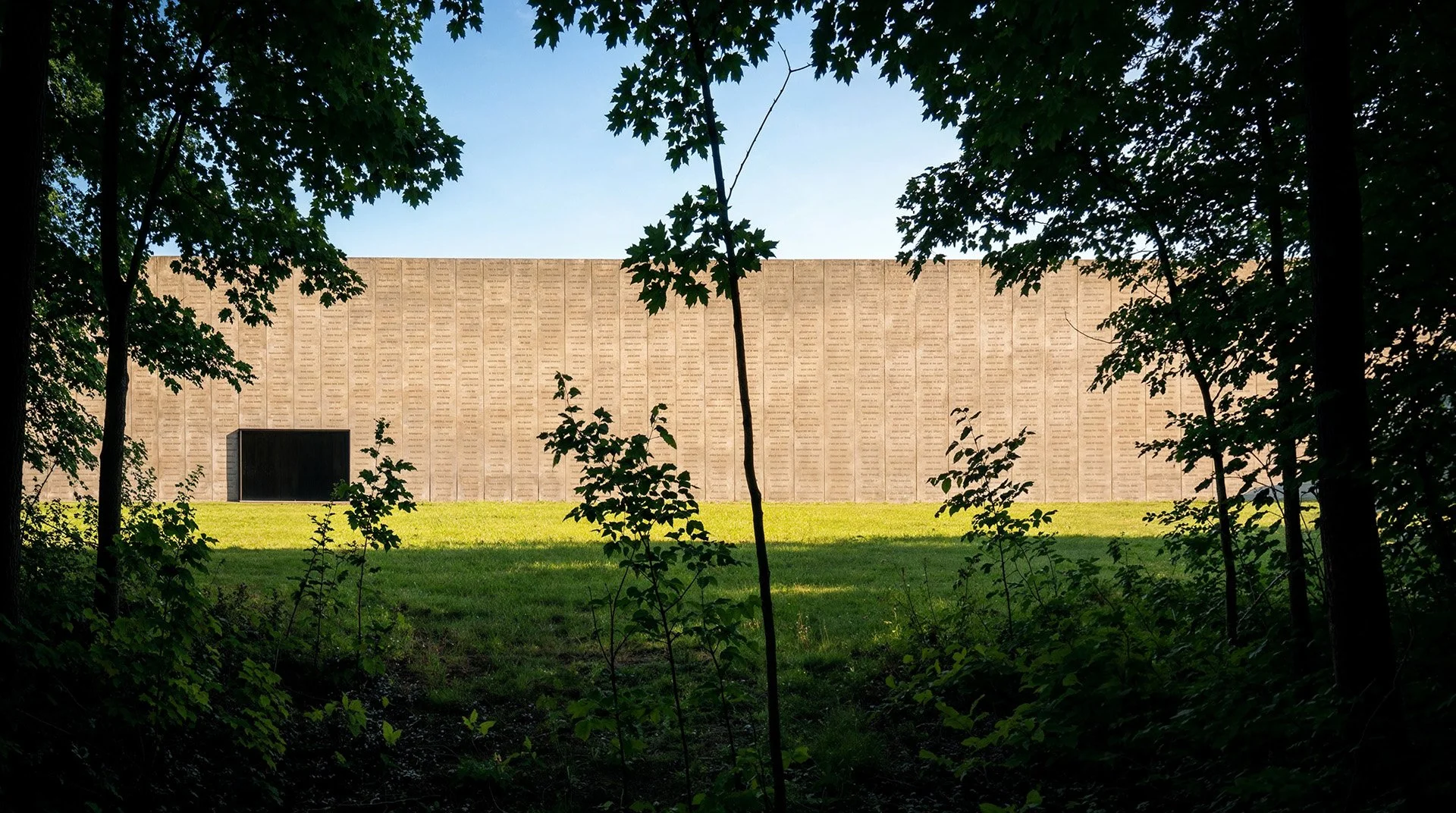 WROT | Hart Island Tumulus: The long wall of the Hart Island Memorial as seen from the tree line.