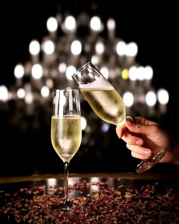 Two glasses of champagne, one being held in a person's hand, with a blurred Christmas tree in the background.