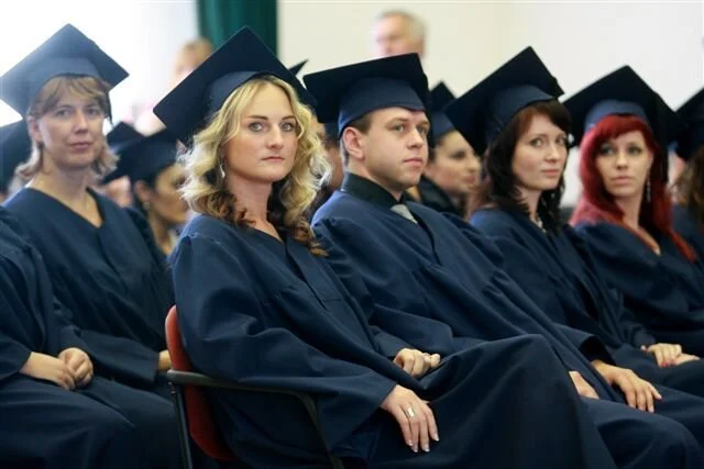 Group of graduates wearing caps and gowns sitting in a ceremony hall.