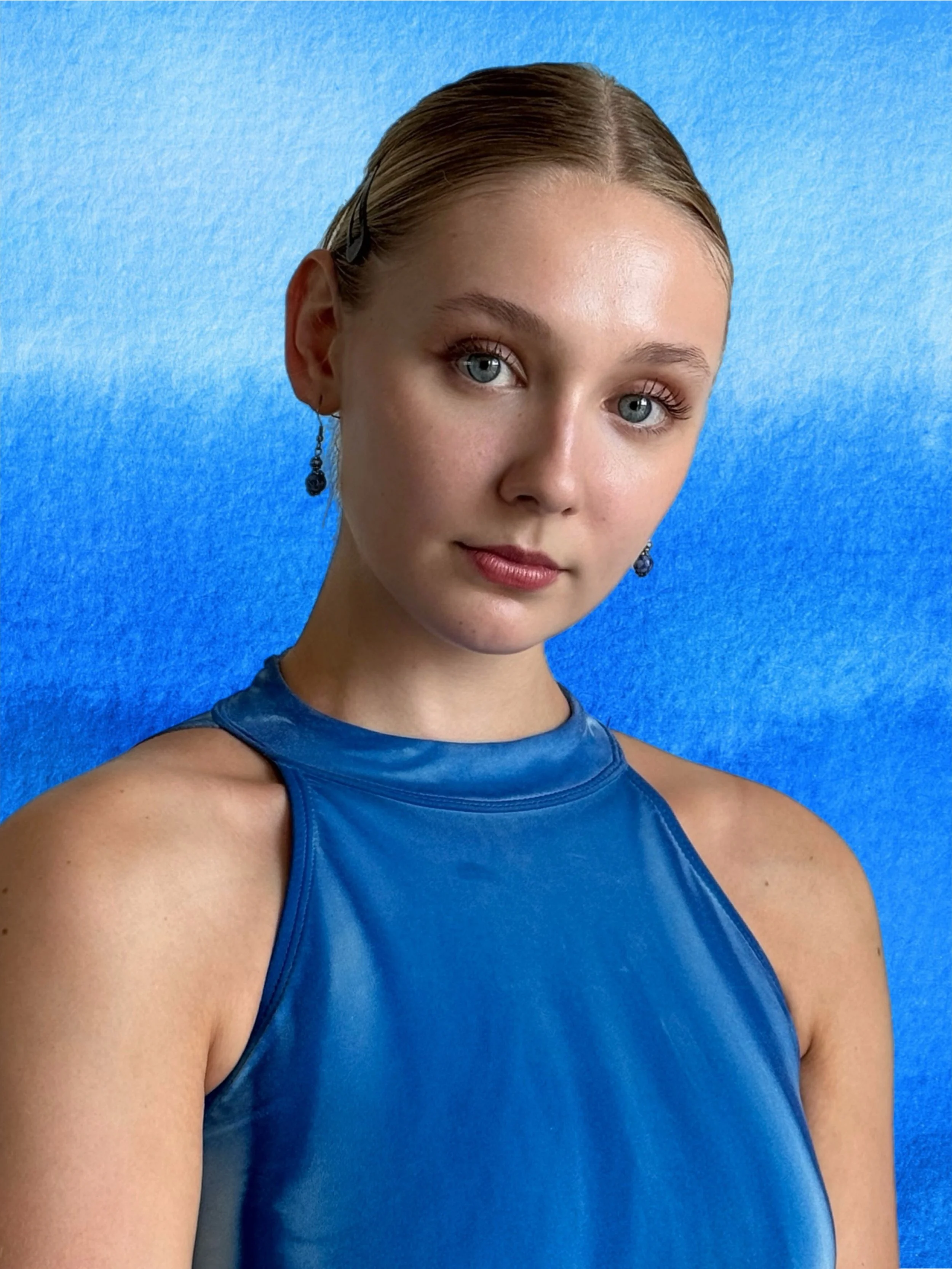 Close-up of a woman with blue eyes, wearing a shiny blue sleeveless top, and earrings, against a textured blue background.