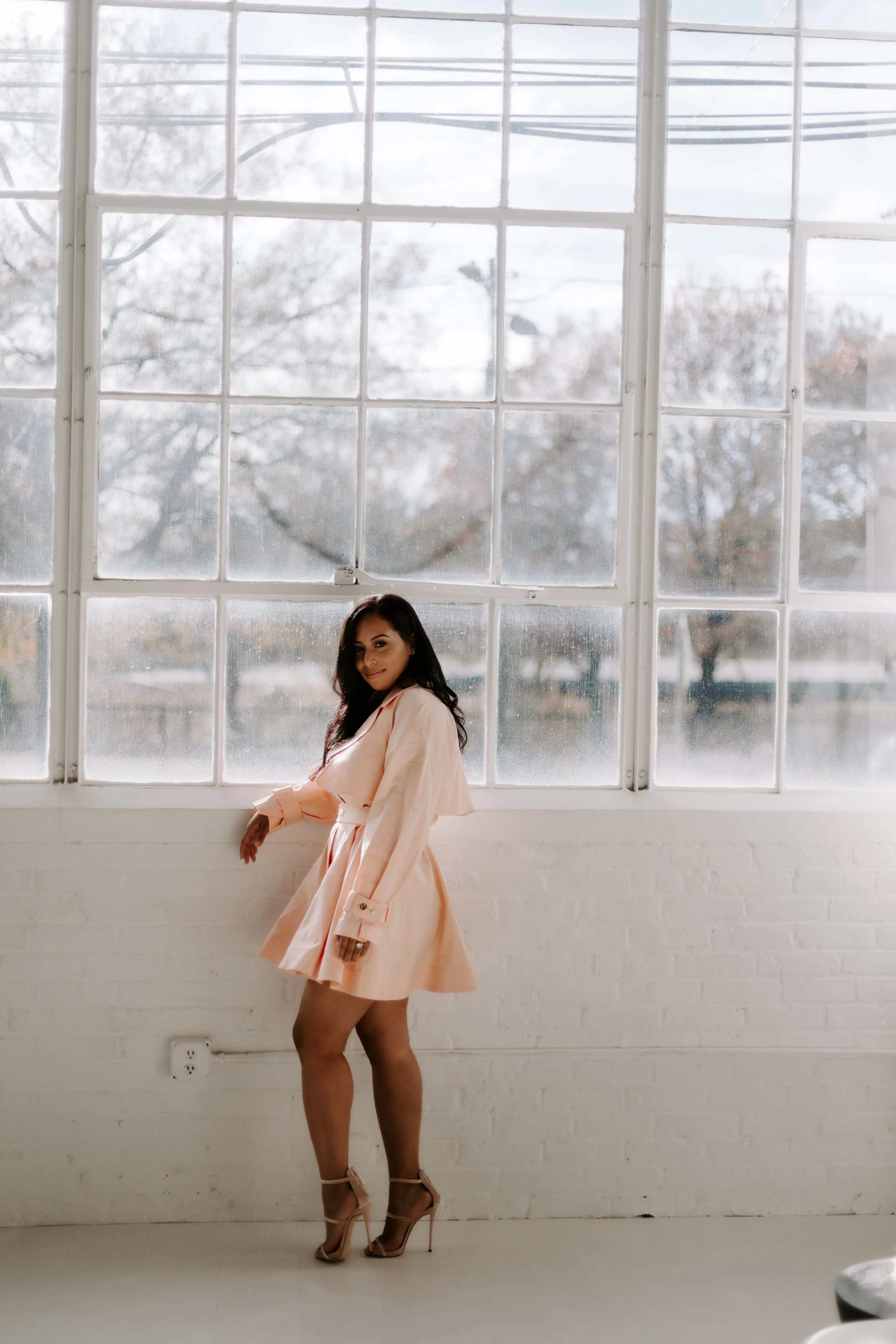 A woman in a peach dress and high heels standing in front of large window with a snow-covered outdoor scene.
