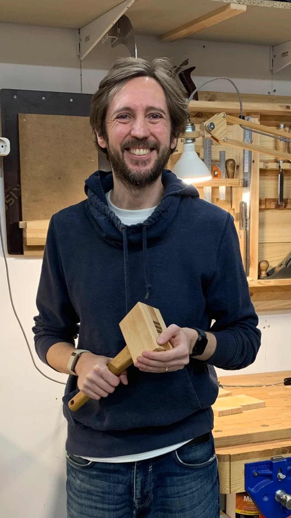 Hombre sonriente sosteniendo un maza de madera recién terminada en un taller de carpintería.