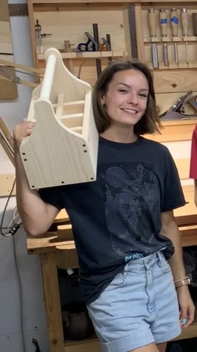 Mujer sonriendo en un taller de carpintería, sosteniendo una caja botellera de madera que acaba de fabricar en un curso.