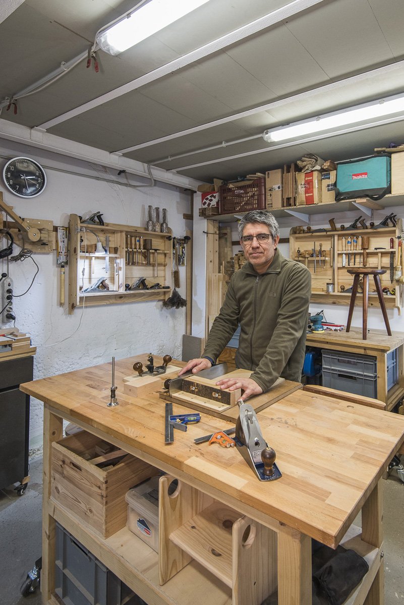 Hombre en un taller de carpintería con herramientas de madera en una mesa de trabajo.