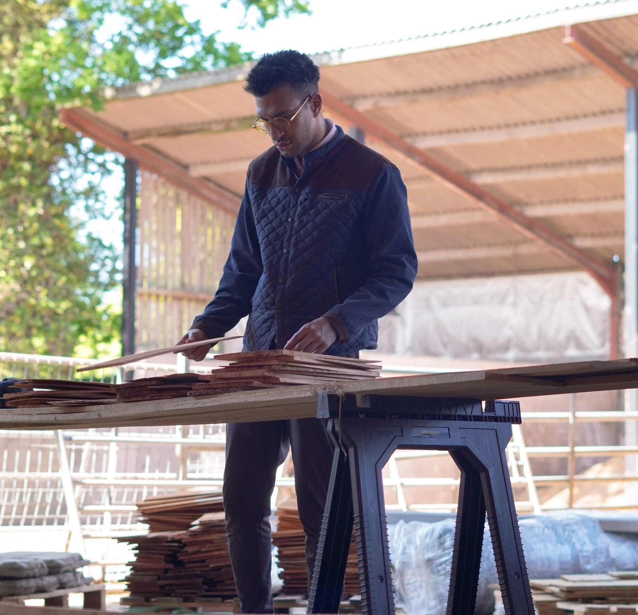Architect inspecting Grade 1 cedar shingles on site during construction of an eco home, assessing material quality prior to installation.
