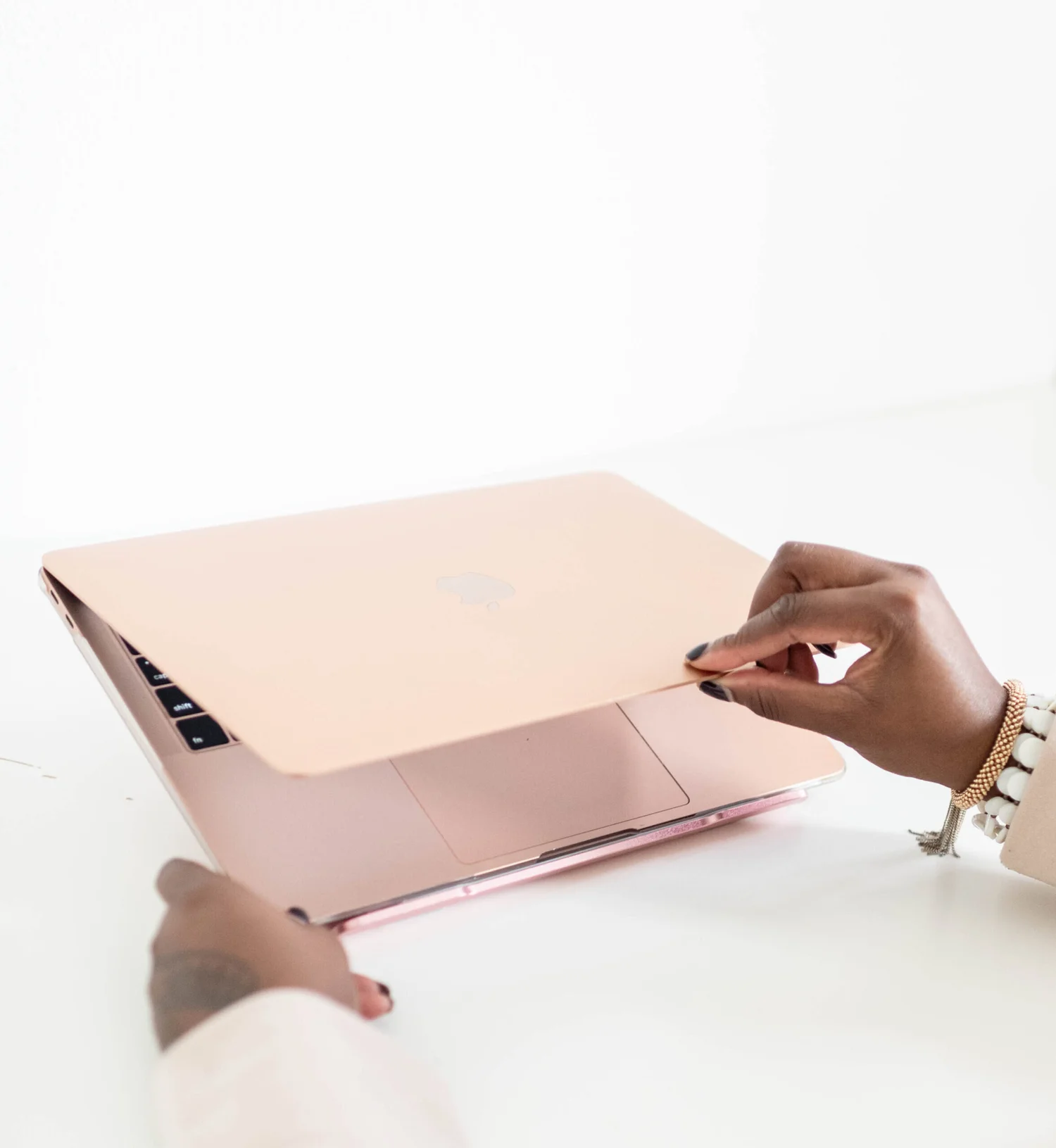 Hands opening a rose-gold laptop on a white desk