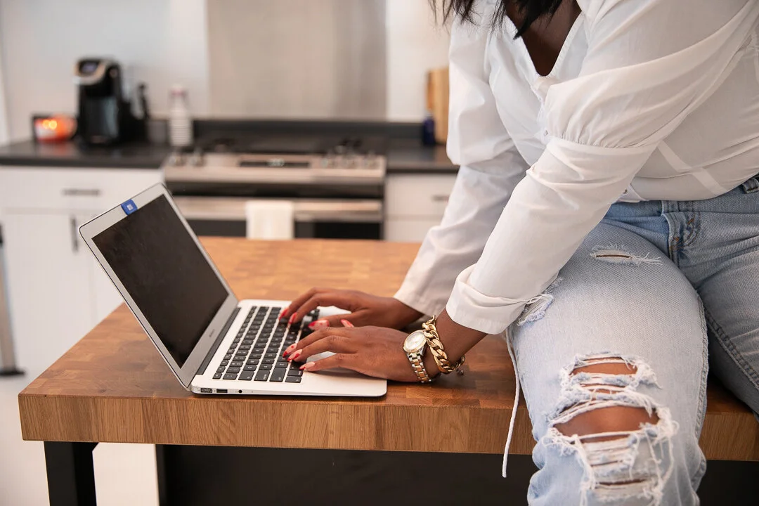 A person typing on a laptop at a wooden kitchen counter