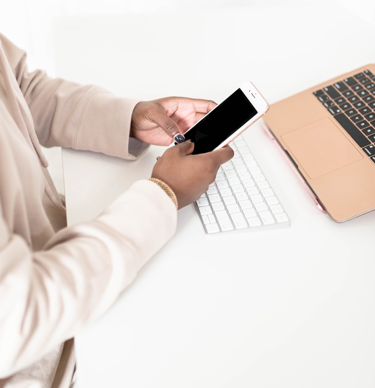 Hands holding a smartphone beside a keyboard and laptop