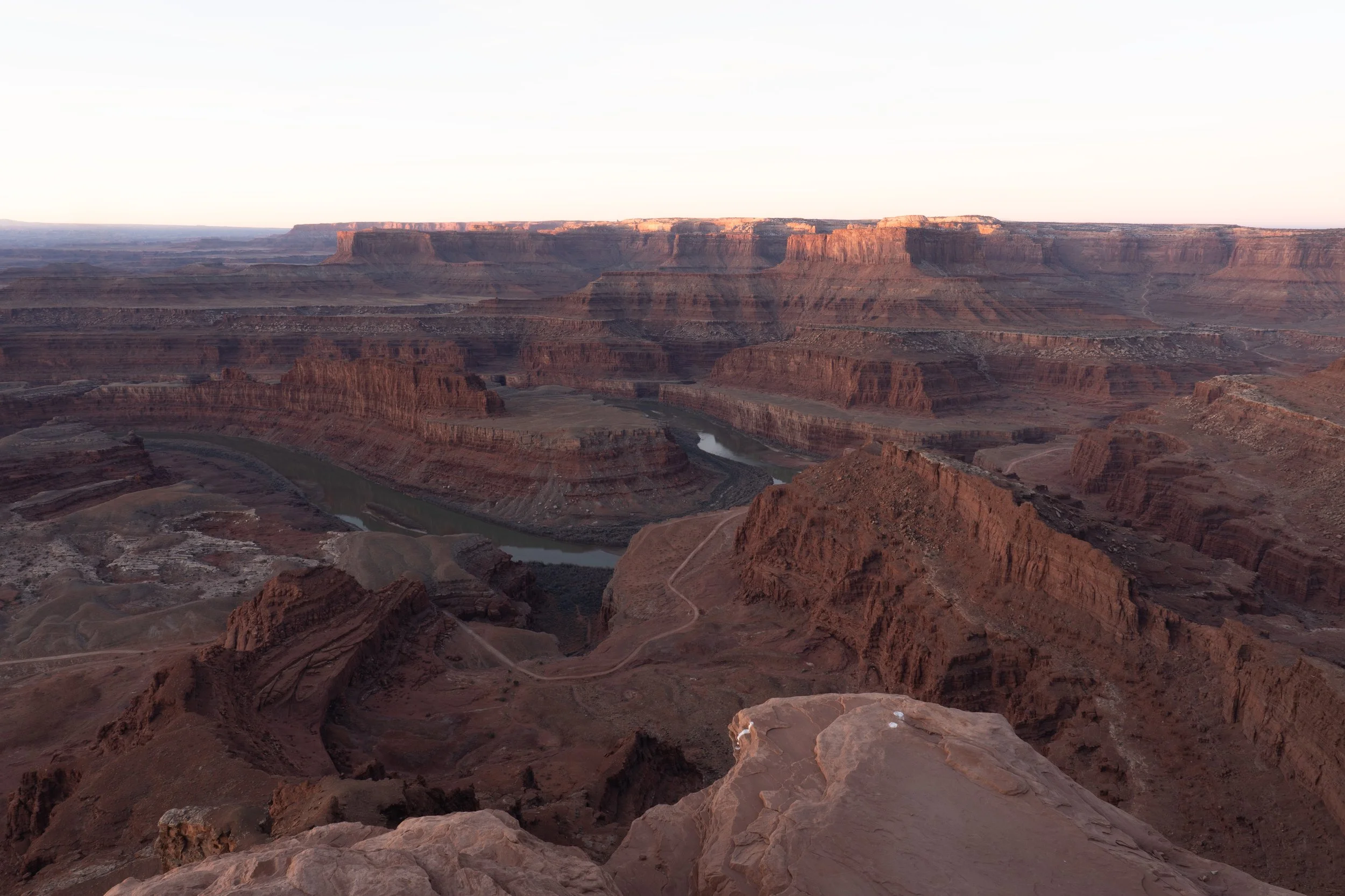 View of the Grand Canyon at sunset with layered red rock formations, a winding river, and a clear sky.