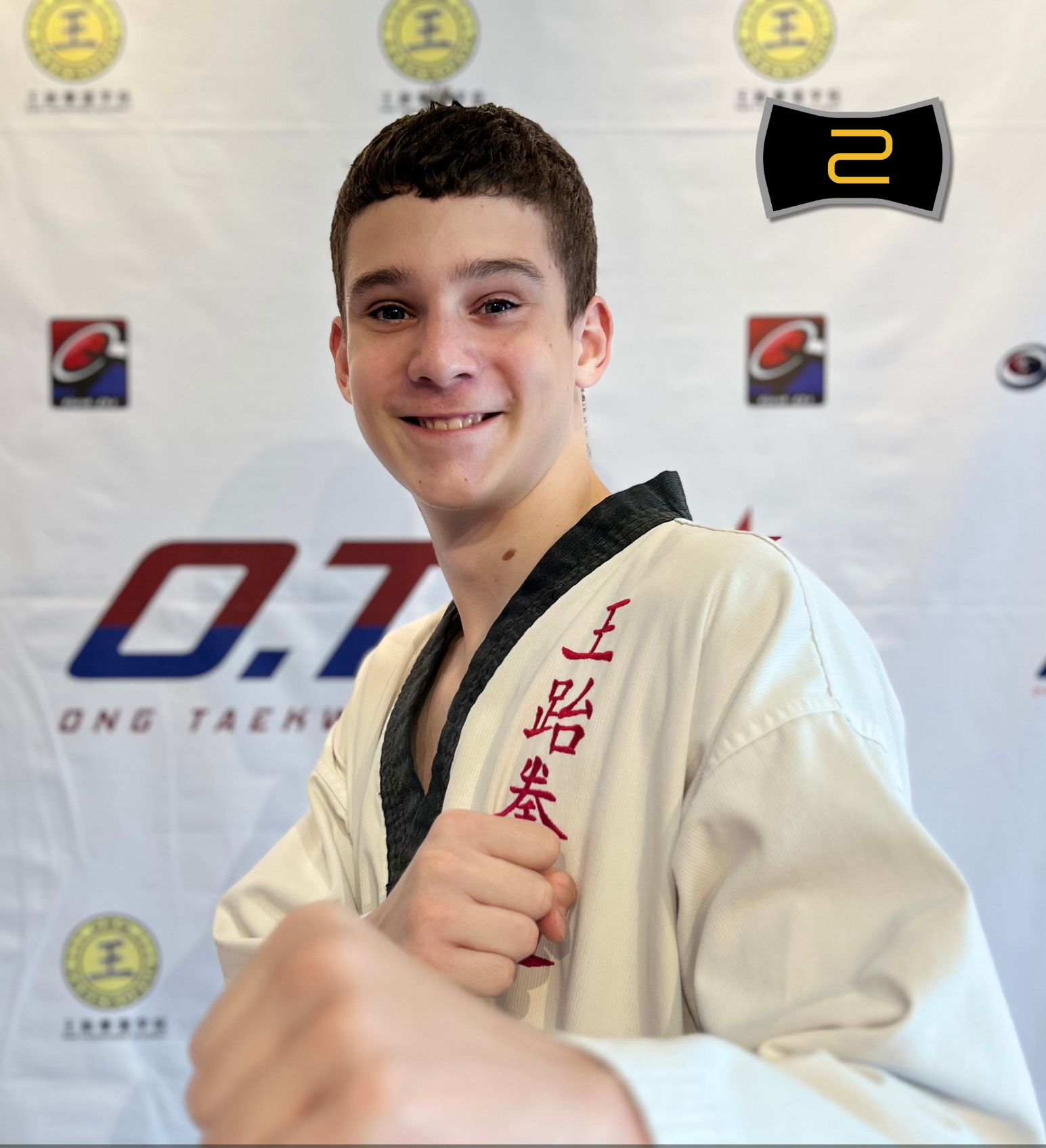 Young man in a taekwondo uniform making a fist and smiling, with background logos and text indicating he is a batch 5 instructor at ONG Taekwondo Academy.