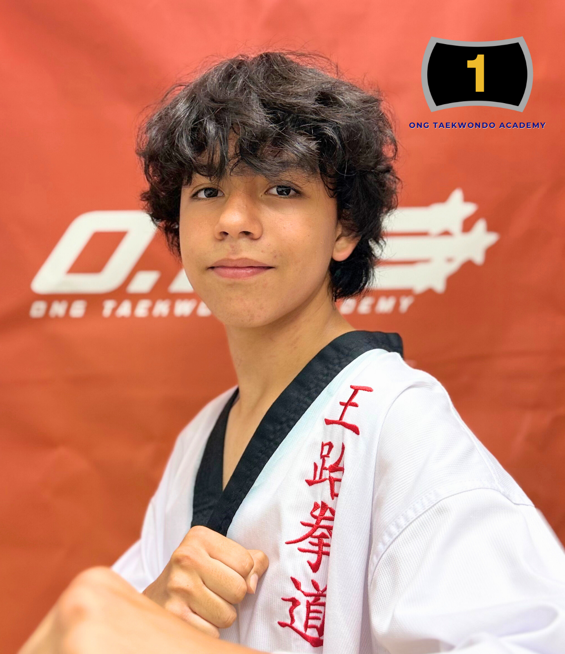 A young person in a taekwondo uniform taking a selfie, with a red background logo for BNE Taekwondo Academy visible behind them.
