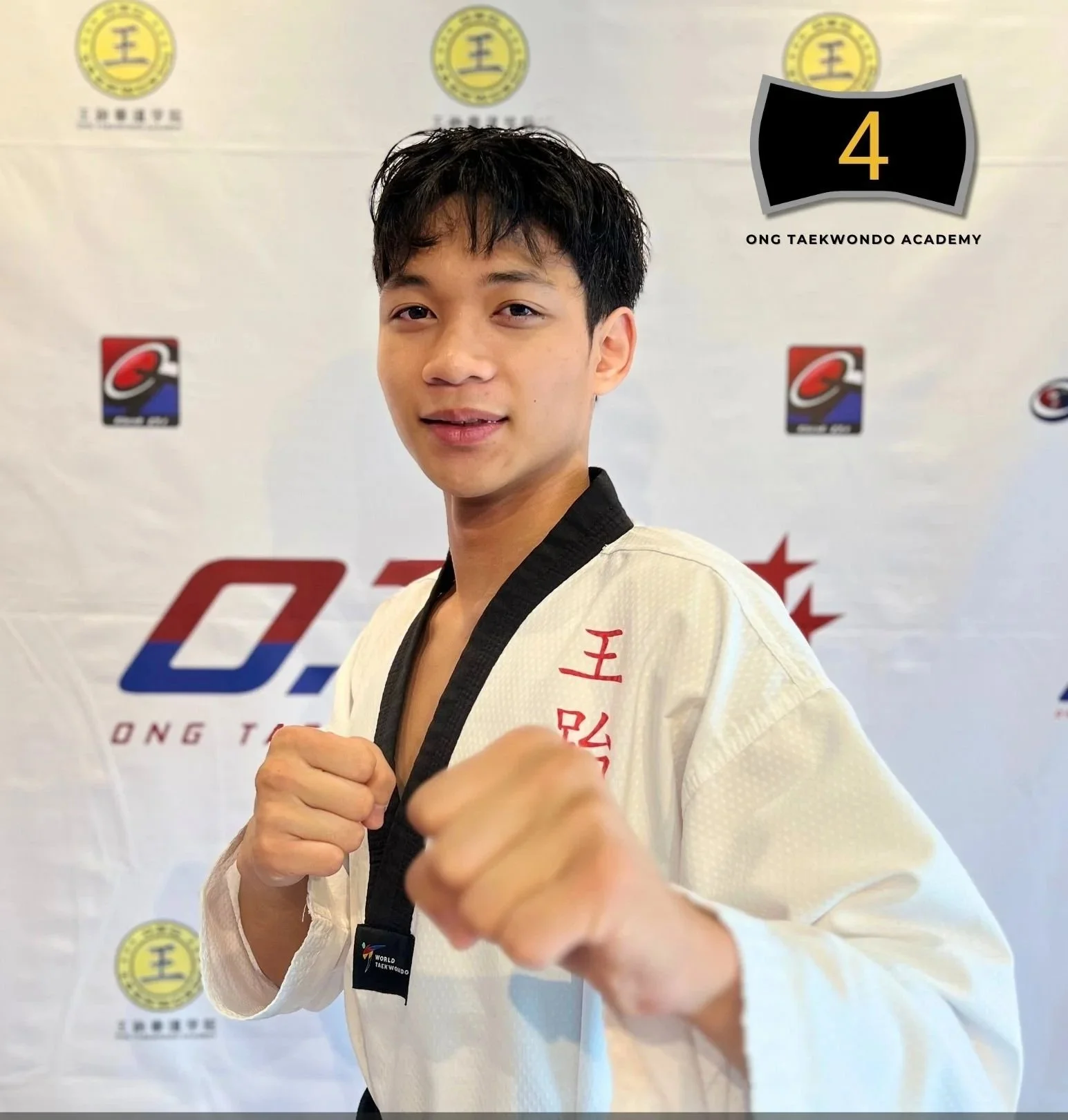 Young male martial artist in a white taekwondo gi with red embroidery, holding a fighting stance in front of a backdrop with logos, with text overlay reading 'Isaac Depakakibo Master Batch 4' and a badge indicating batch 4.