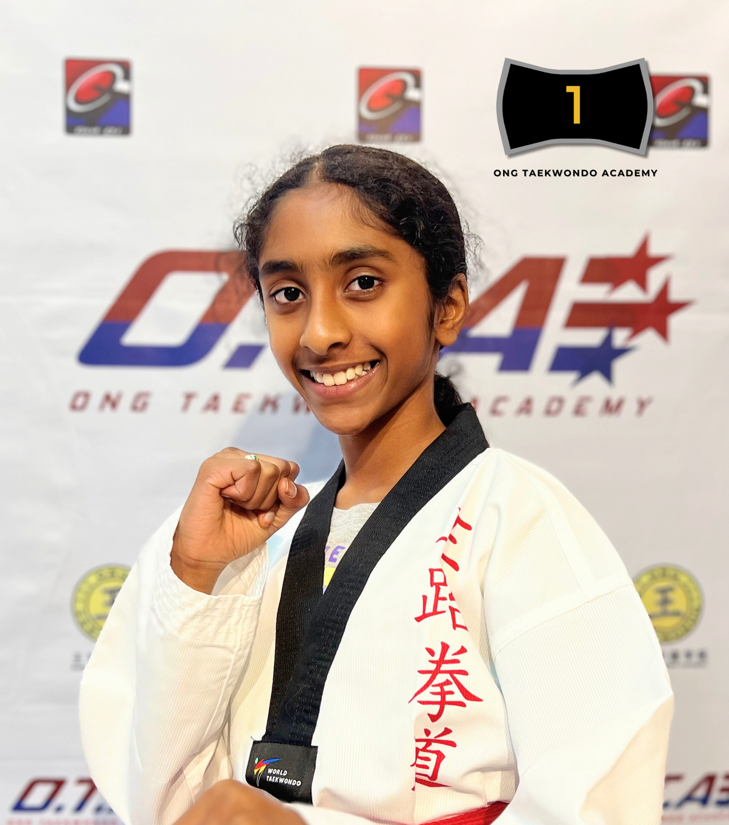 Young girl in a white taekwondo uniform with red and black belts, smiling and showing a fist, with a backdrop displaying taekwondo logos and text indicating she earned a black belt in 2024.
