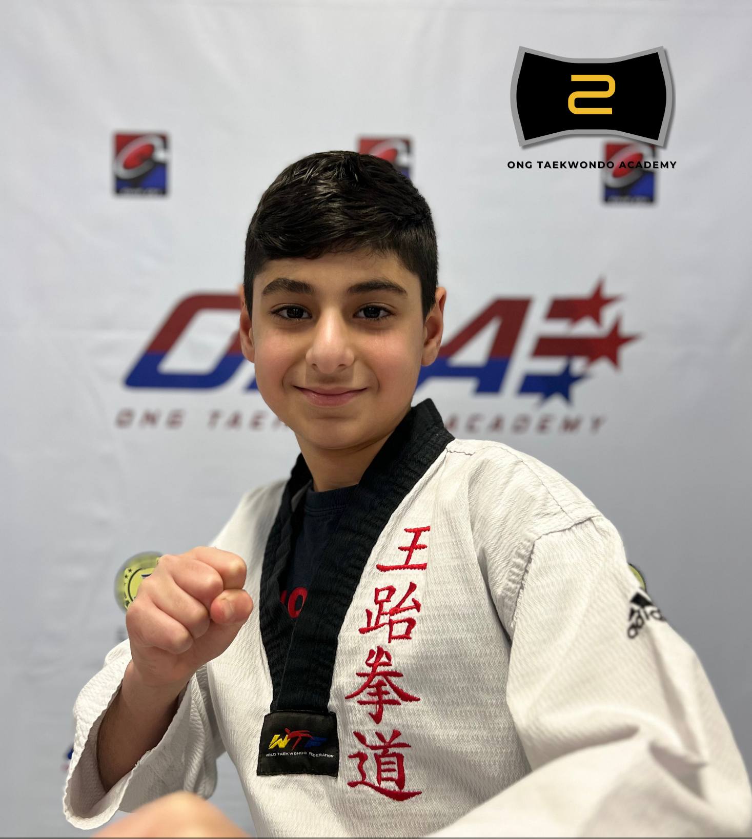A young male martial artist wearing a black belt and a white gi with red Chinese characters, posing confidently with a clenched fist in front of a backdrop that features the logo for Onn Taekwondo Academy and other sports logos.