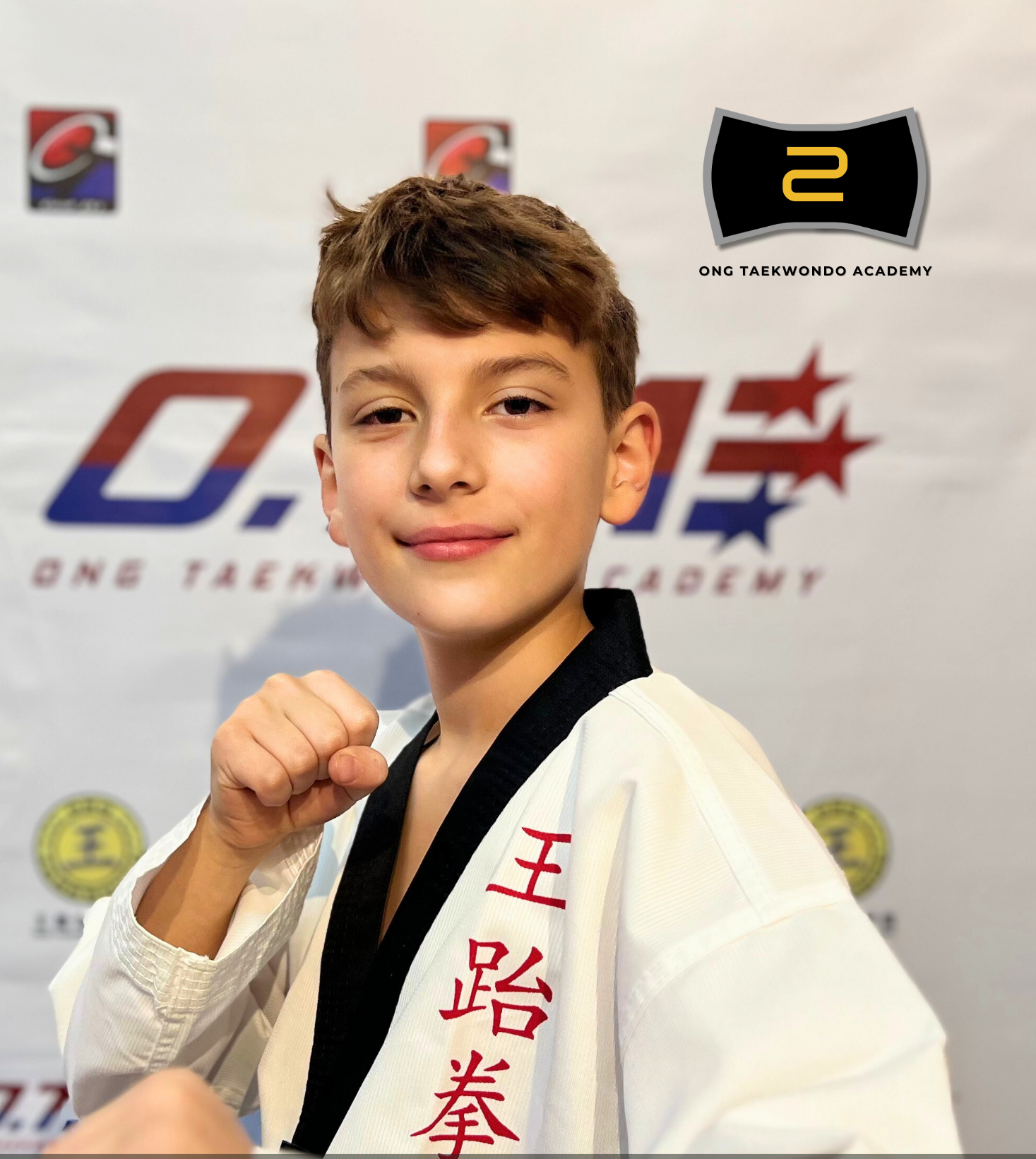 Young boy in a martial arts uniform making a fist, smiling, in front of a backdrop with martial arts and academy logos, with text overlay indicating his name Benjamin Dojka and achievement of black belt in 2024.