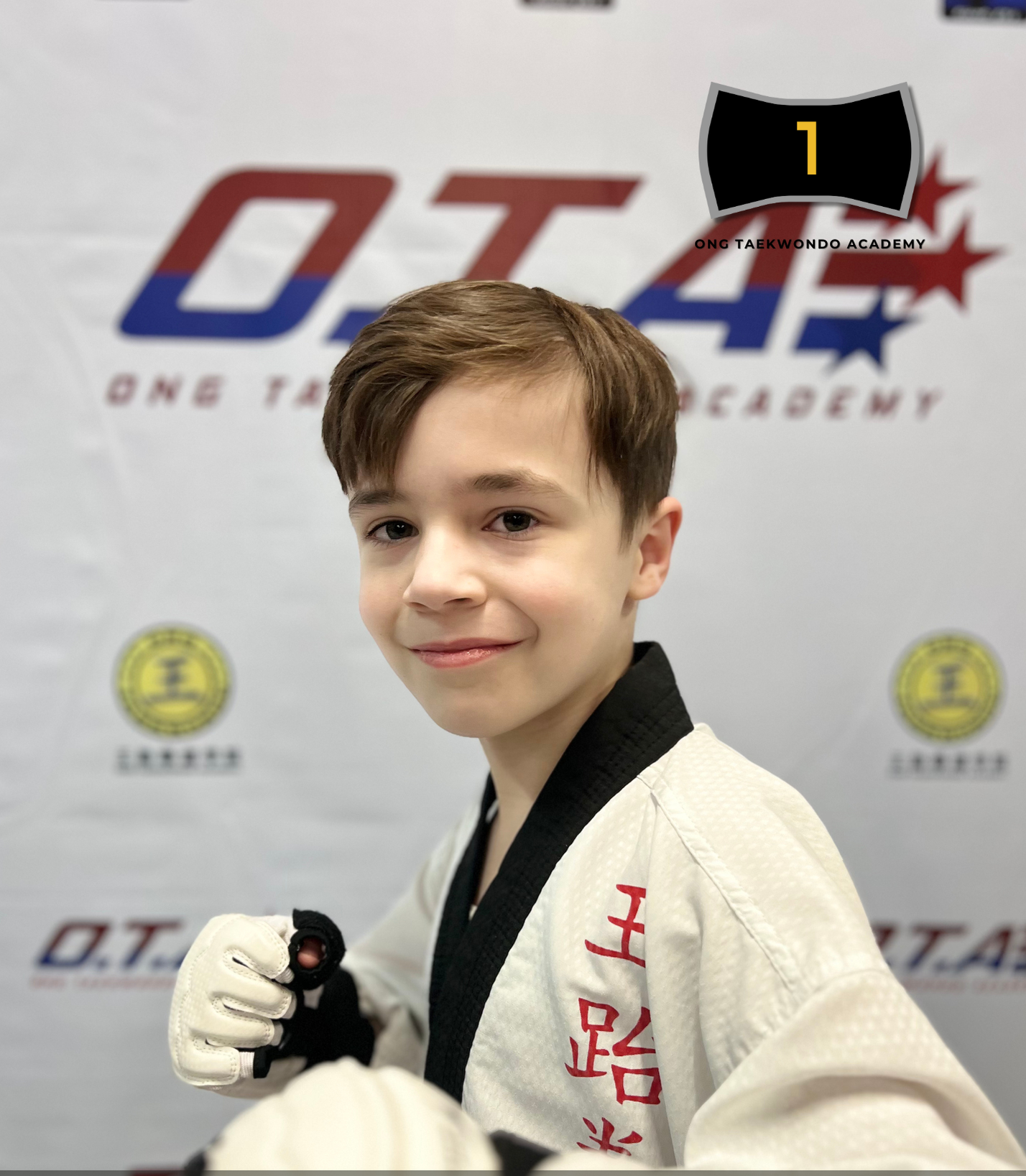 Young boy in a martial arts uniform with a black belt, making a fighting stance at a taekwondo academy event in 2022.