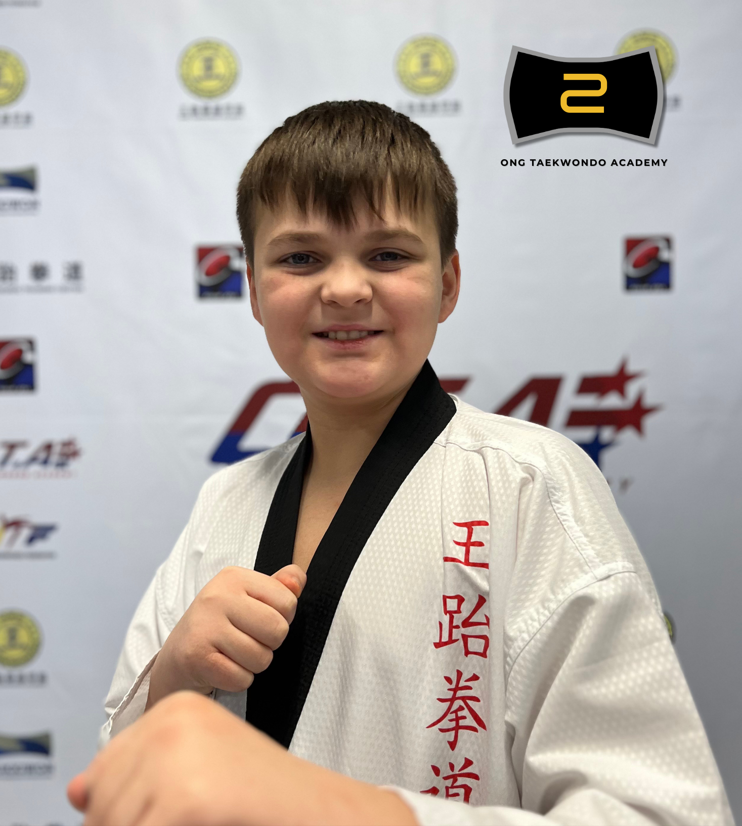 Young boy in martial arts uniform showing a fist, standing in front of a backdrop with logos. Text overlay: 'Adam Horodechny Black Belt Year 2024' with a TaeKwonDo emblem.
