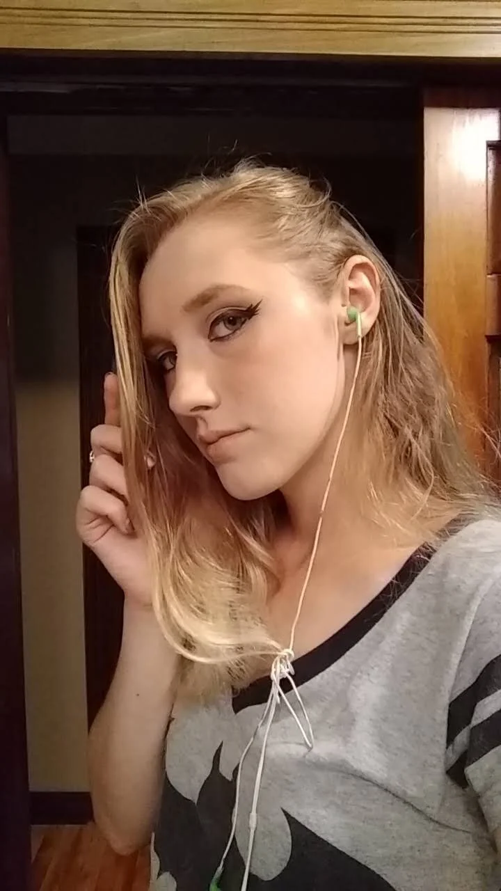 Young woman with blonde hair wearing earphones taking a selfie indoors.