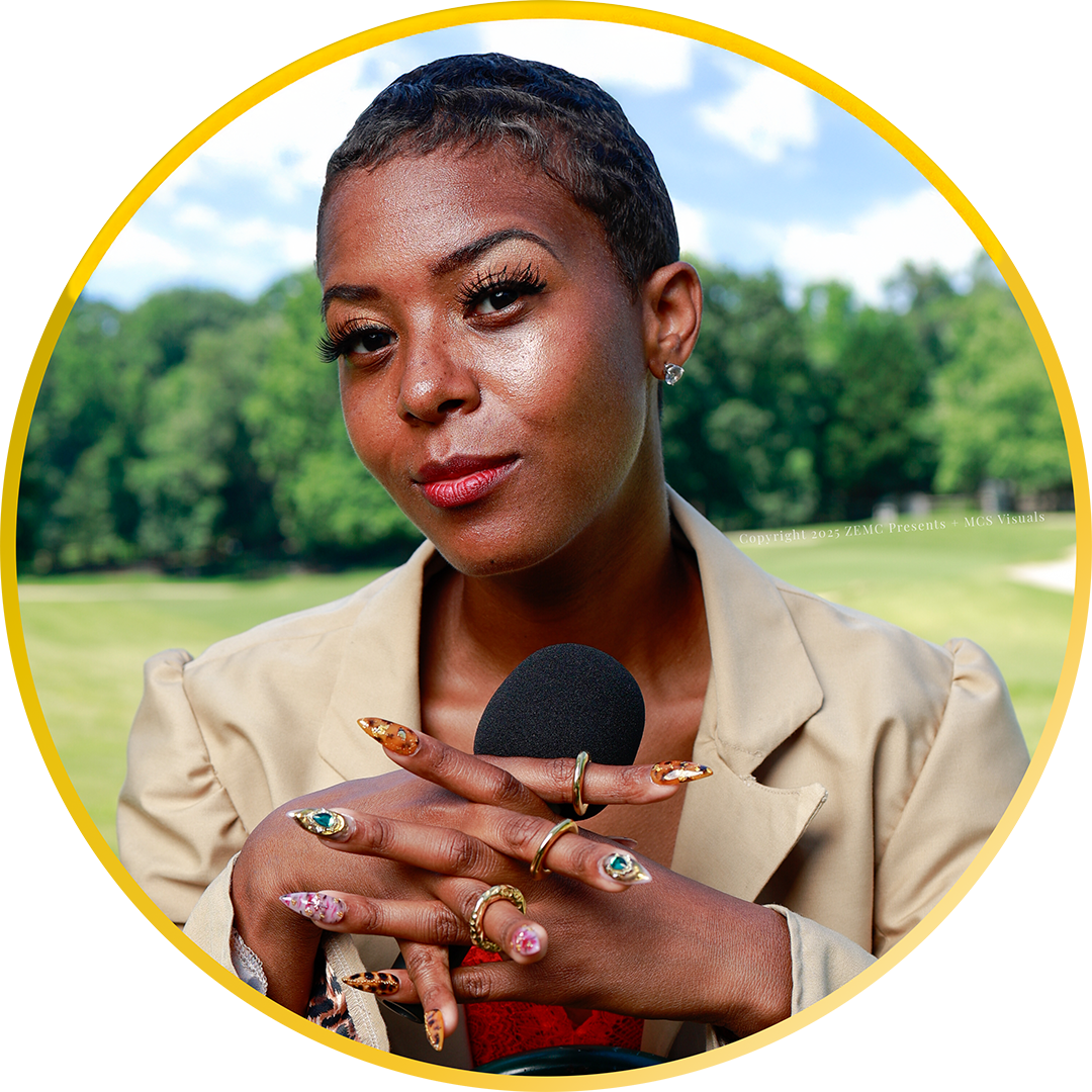 A portrait of Zena C. holding a microphone while wearing a tan blazer and heavily embellished fingernails in front of a grassy meadow with a full treeline and a beautiful partially cloudy sky.