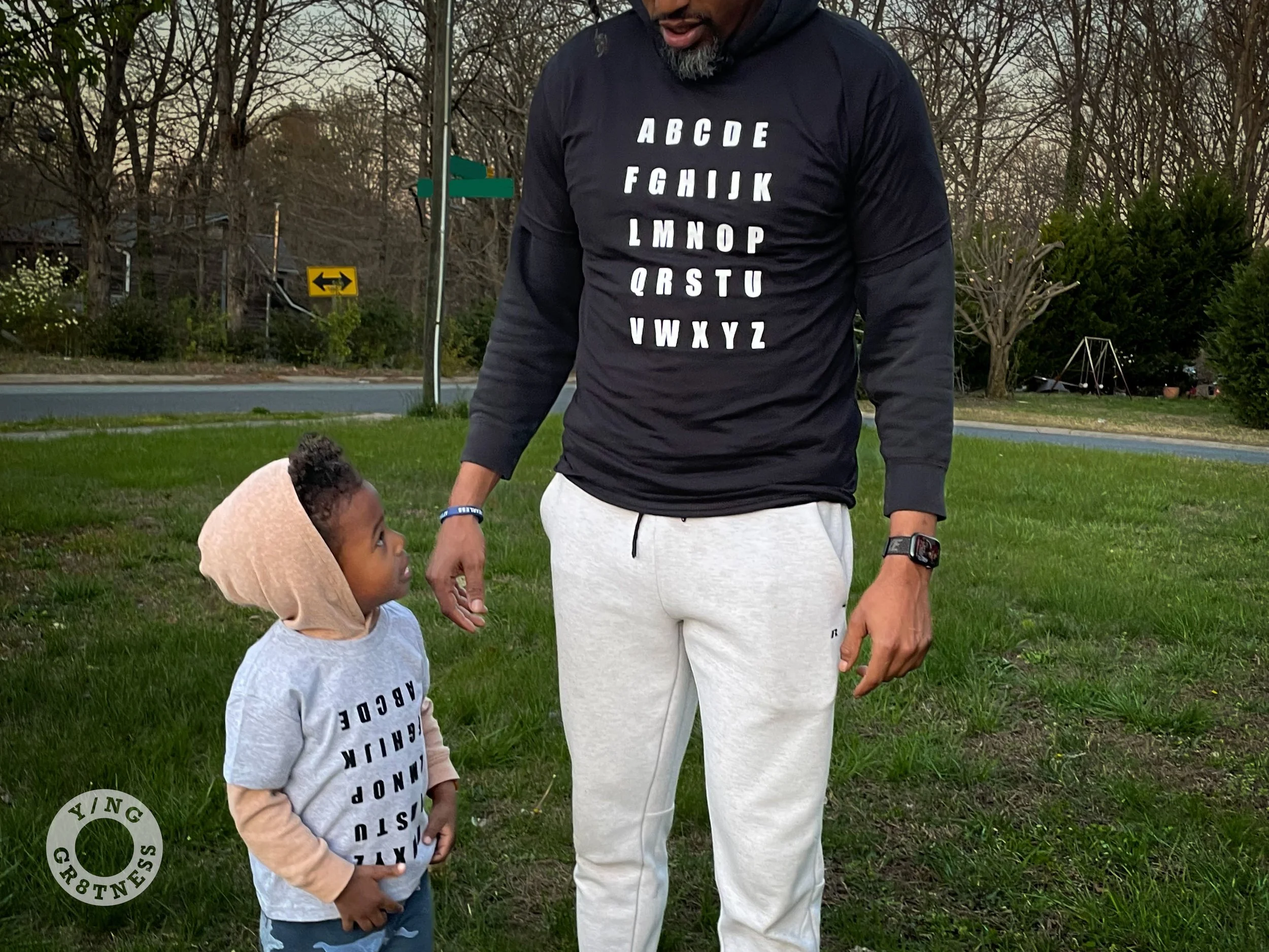 A father and son duo standing in the front yard while the son is wearing the grey ABC Tee and the father is wearing the Black Alphabet Graphic Tee.