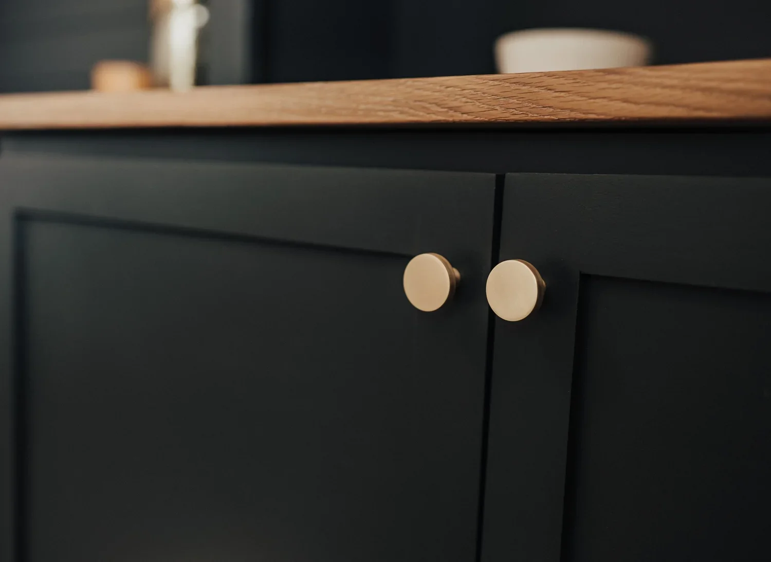 Close-up of a black kitchen cabinet with two cream-colored round knobs and a wooden countertop.