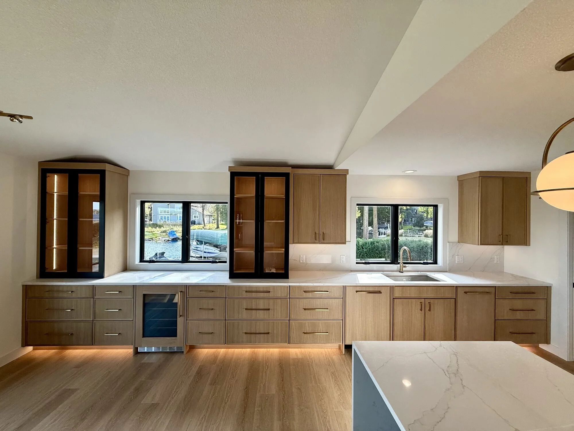 White oak kitchen with lit glass-front upper cabinets and a lake view, part of a whole-home cabinetry project in Forest Lake, MN