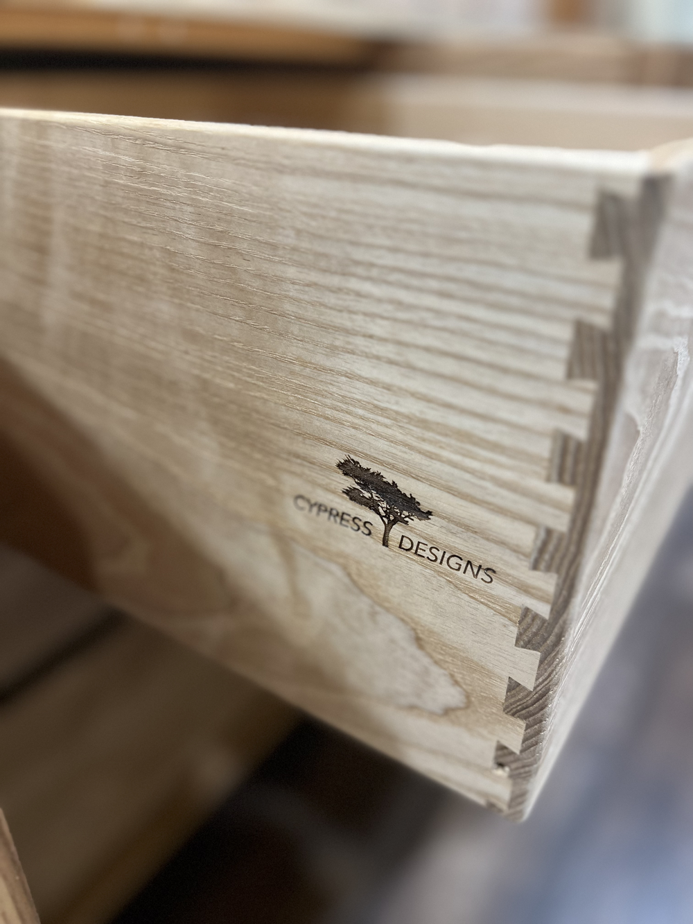 Close-up of a wooden box or crate with the logo 'Cypress Designs' and an image of a cypress tree on it.