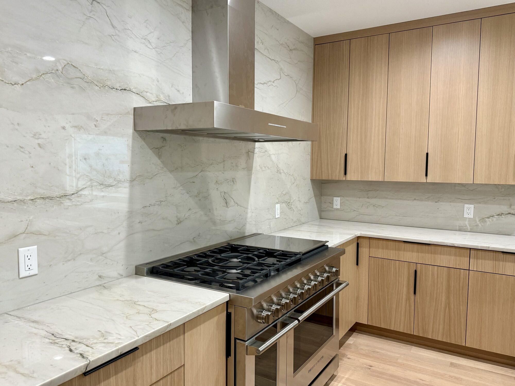 Grain-matched rift-sawn white oak slab cabinets with a quartzite slab backsplash and range, Blaine, MN