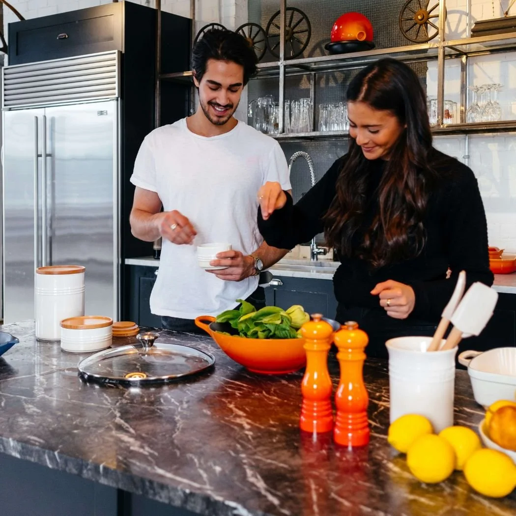 Man and woman cooking in kitchen with stainless steel refrigerator behind them