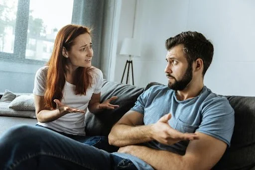 Woman with hands out arguing with man on couch