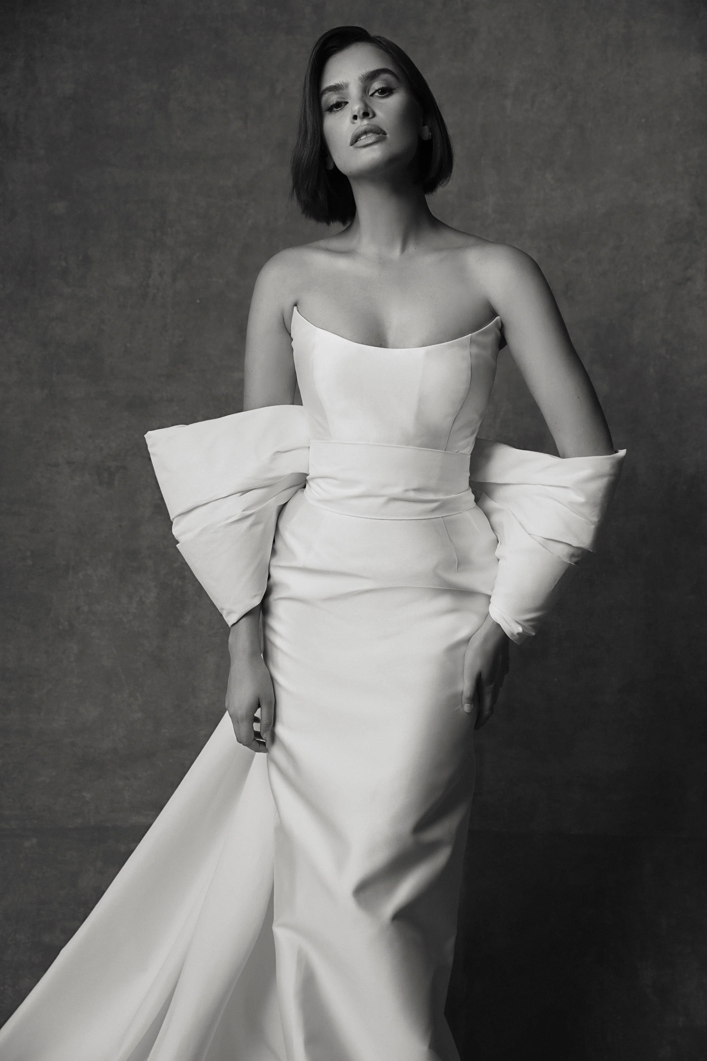 Black and white photo of a woman in an elegant strapless gown with large bow details on the sleeves, posing against a plain background.