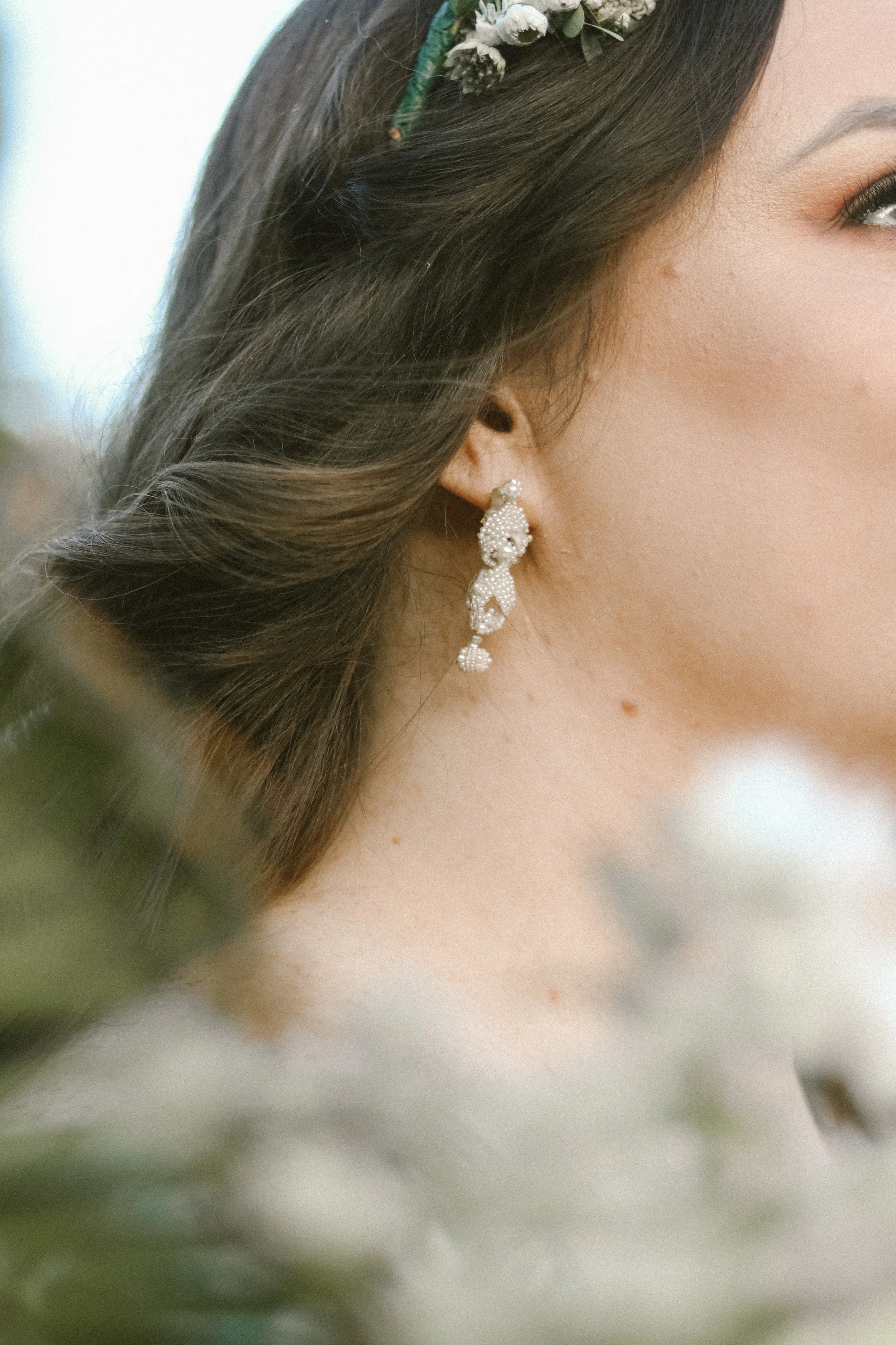 Close-up of a woman's face showing her ear with a sparkling earring, dark brown hair with a floral headband, and part of her eye and cheek.