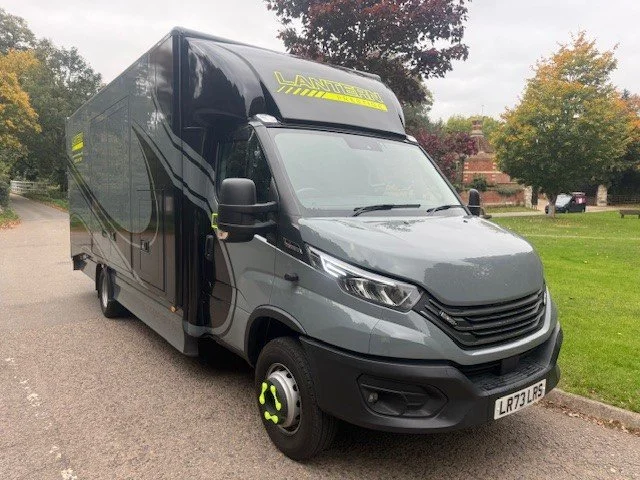 Black and gray moving truck with yellow accents parked on a driveway near a grassy area with trees.