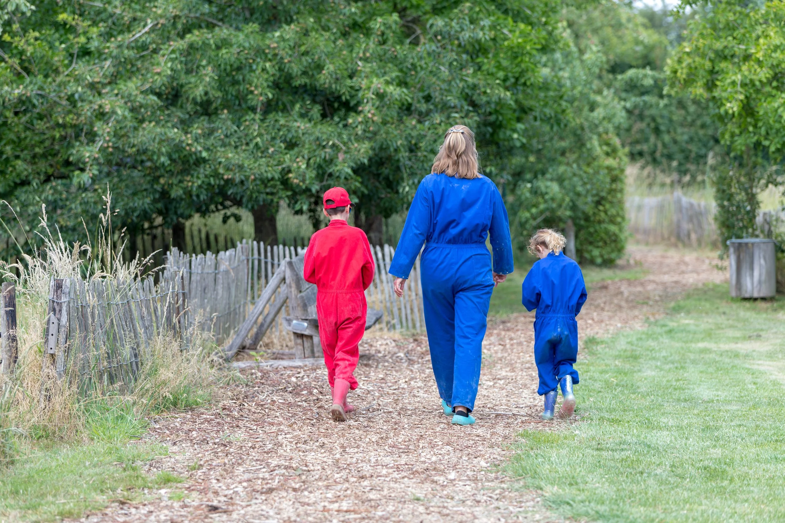 Drie mensen in regenpakken lopen samen op een smal pad door een groen landschap met bomen en struiken.