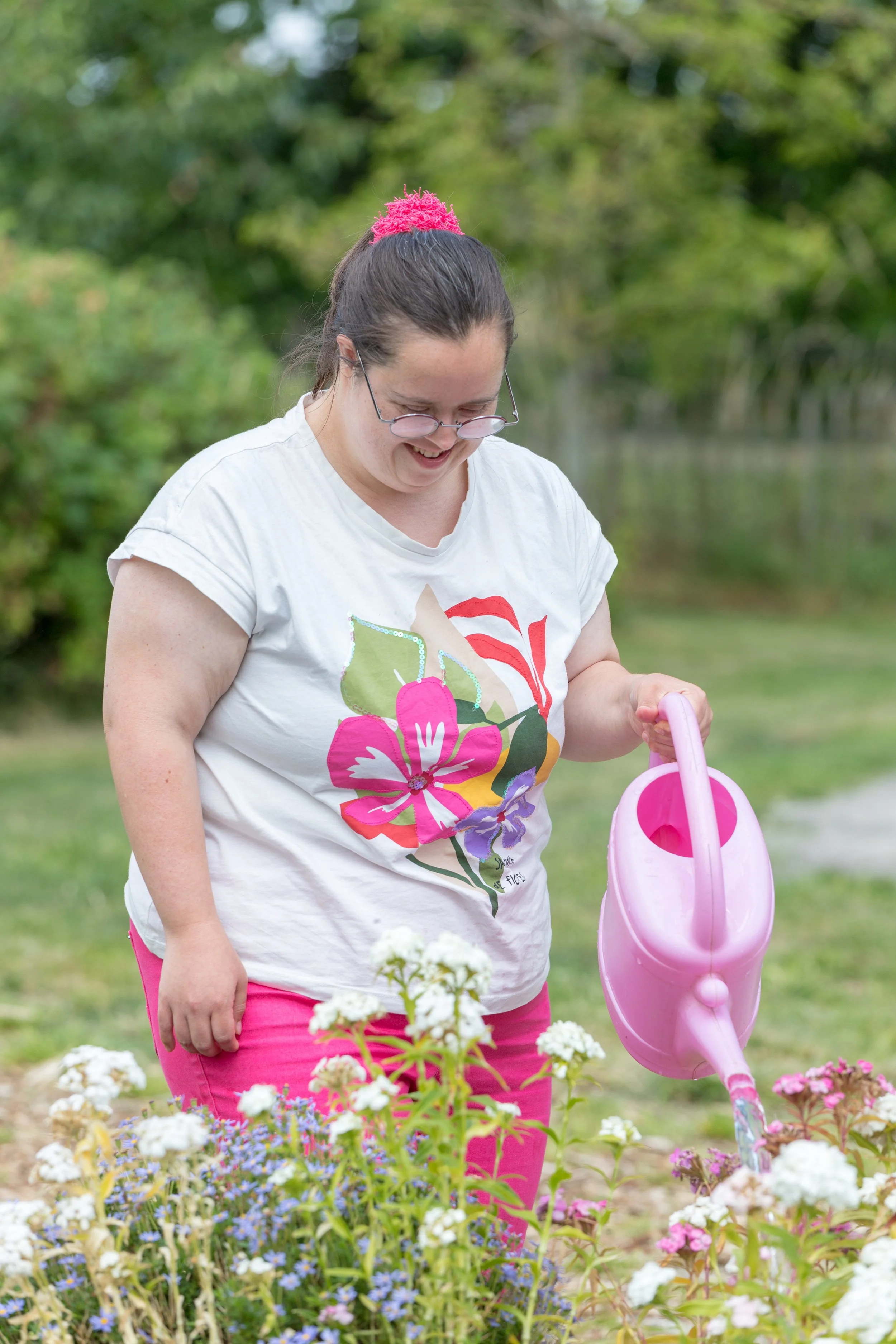 Vrouw met een lach, water gietende in een moestuin met kleurrijke bloemen, groene achtergrond.