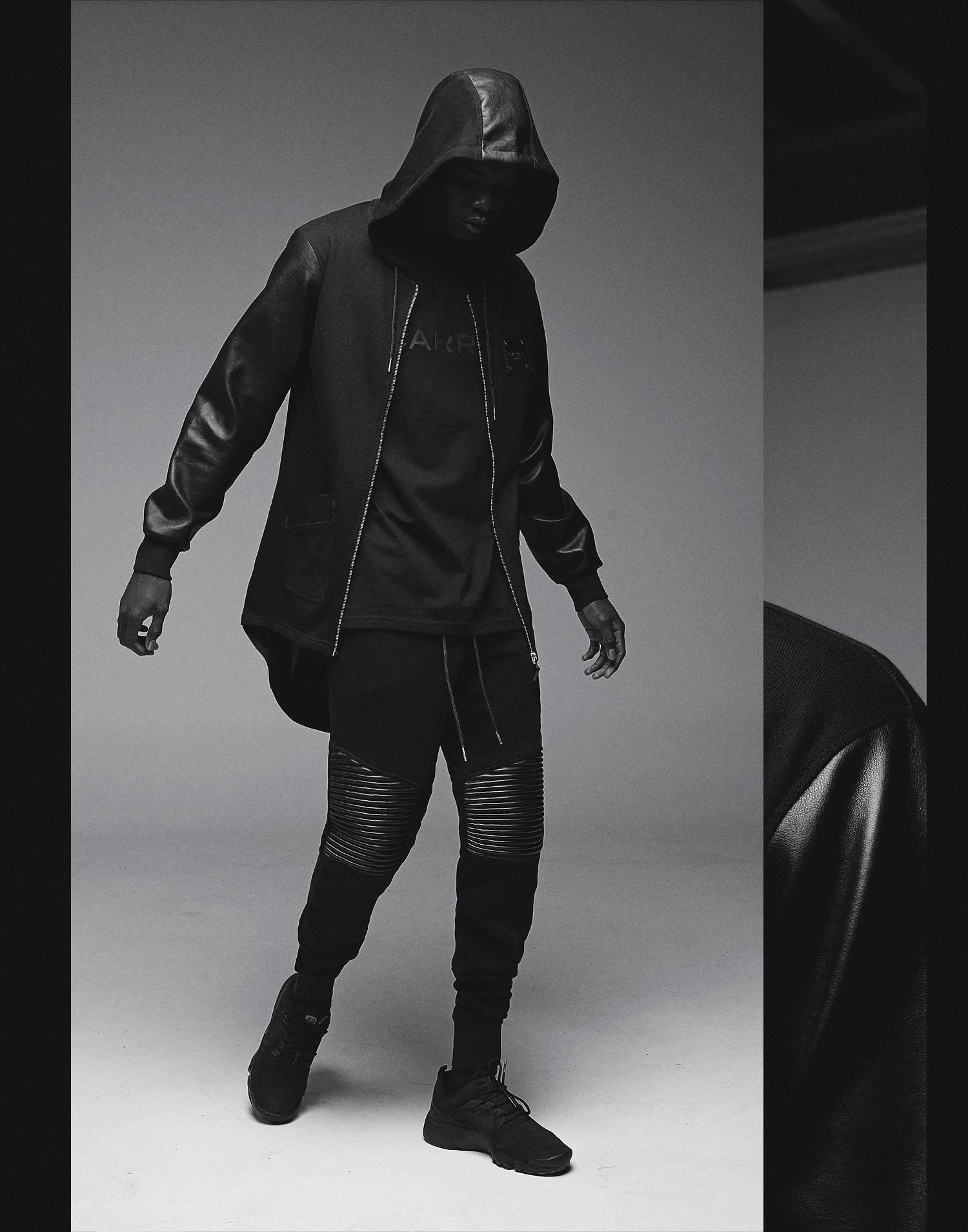 Person dressed in black athletic wear with a hood, standing against a plain background.