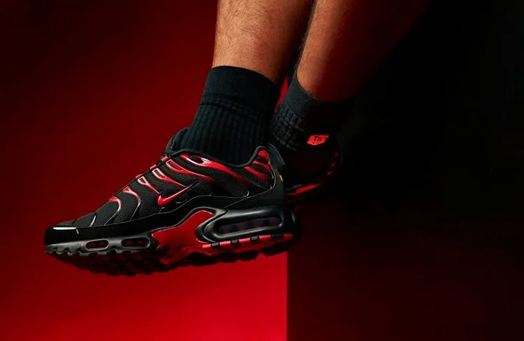 Close-up of a person's legs wearing black and red Nike sneakers and black socks, against a red and black background.