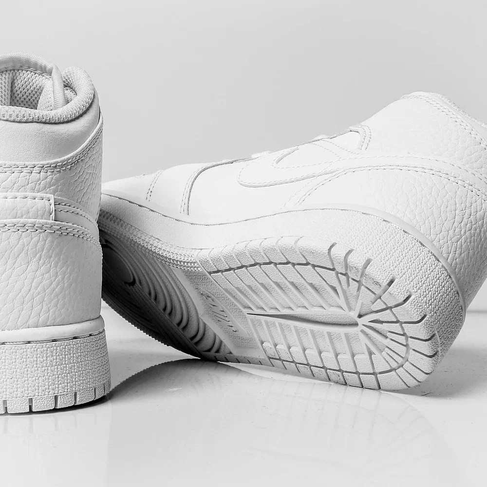 Close-up of a pair of white athletic shoes, with one shoe resting upside down showing the tread on the sole.
