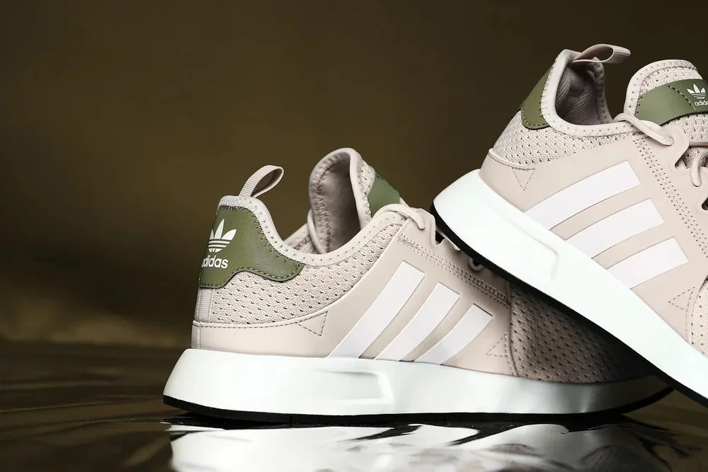 A pair of Adidas sneakers with beige and green details on a reflective surface.