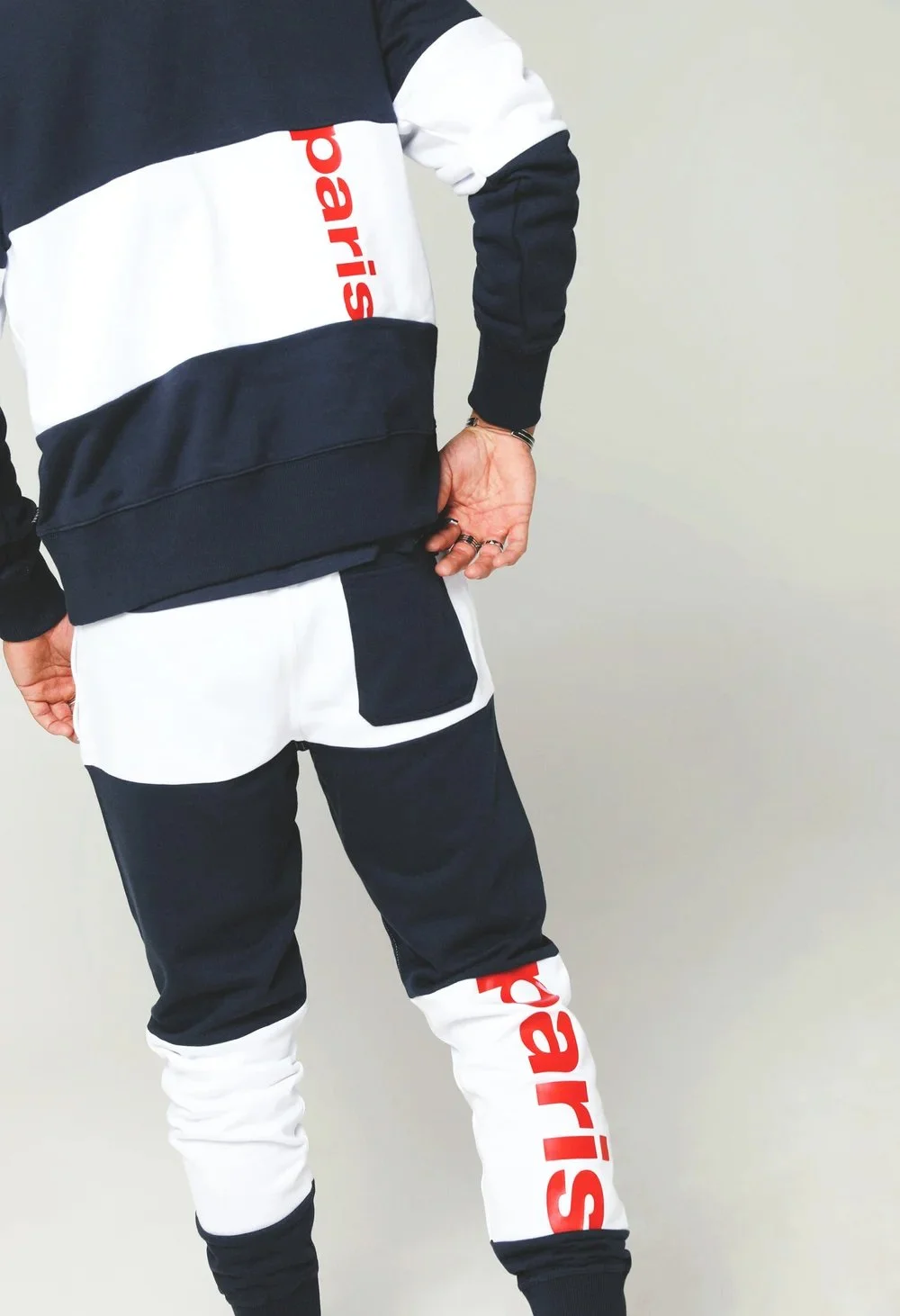 Person wearing black, white, and red logo branded activewear, with the word 'Parisd' visible on the shirt and track pants, standing against a plain background.