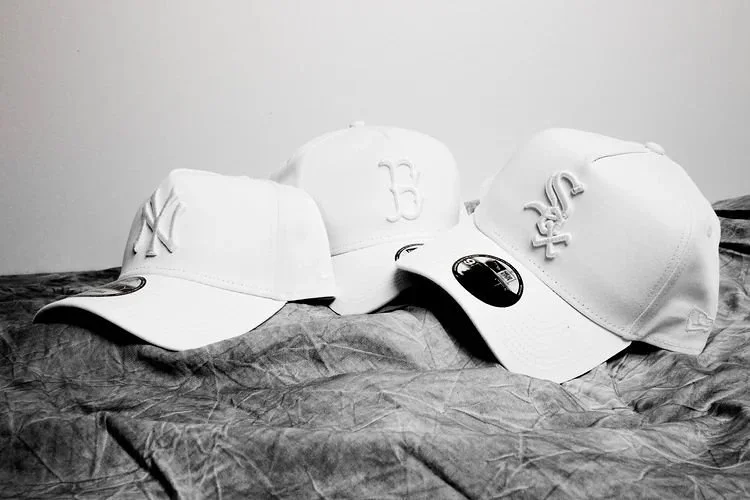 Four white baseball caps with different team logos on a crumpled surface.