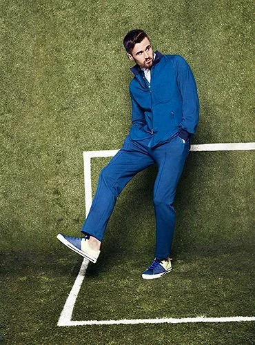 A man in a blue tracksuit standing on a tennis court, with a portion of the court's white boundary lines visible.