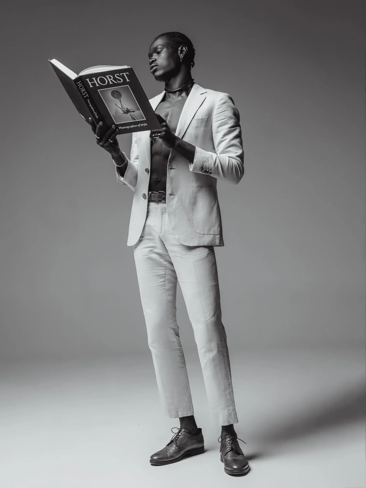 A person dressed in a light-colored suit reading a book titled 'HORST' against a plain background.