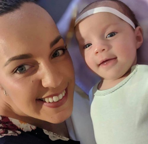 A woman and a baby lying in bed, smiling at the camera.