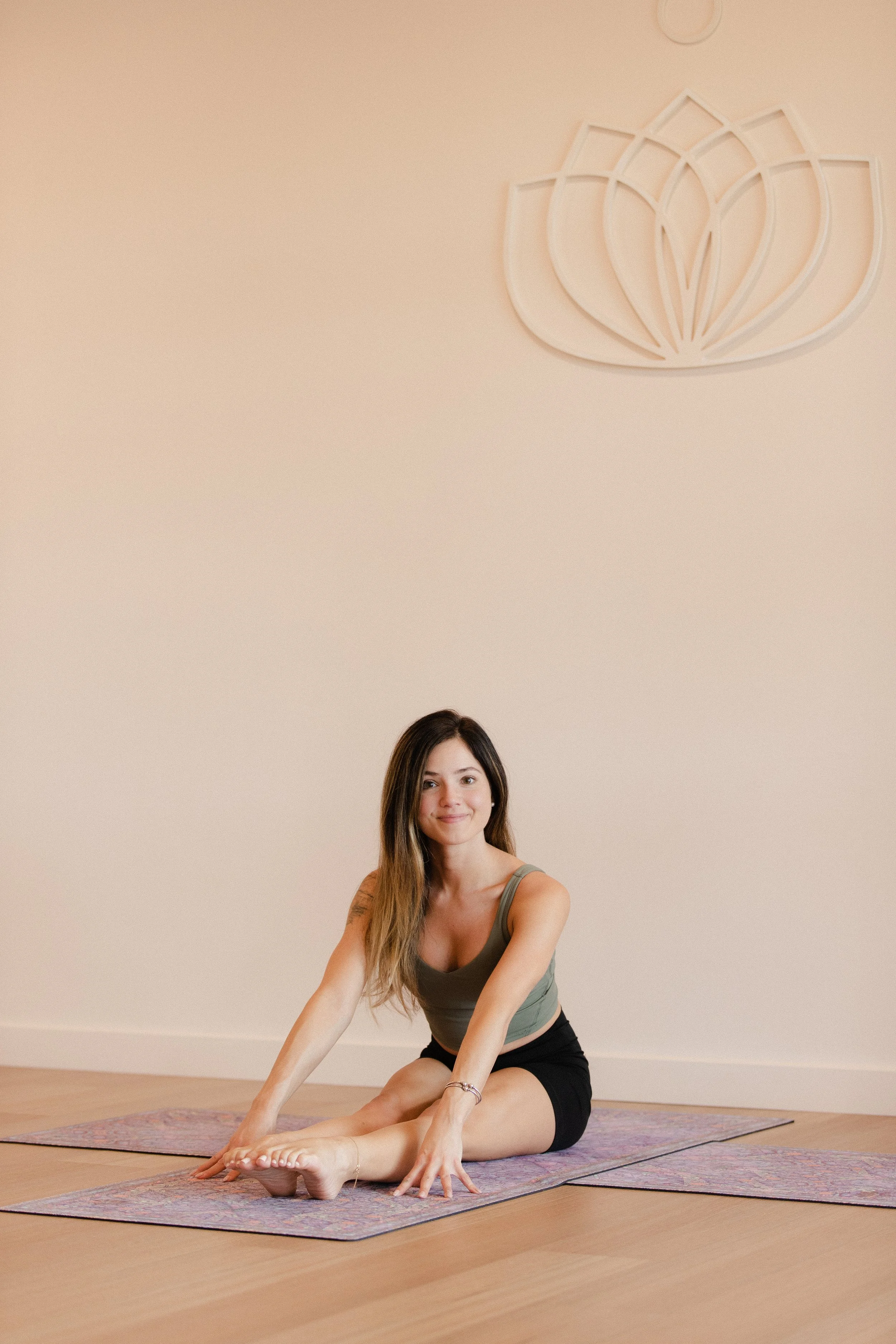 Young woman practicing yoga on mat in a studio with beige wall and lotus flower wall art.